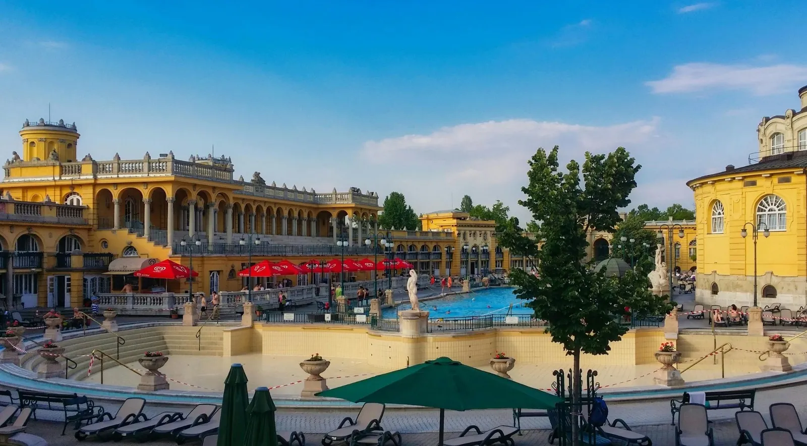 Széchenyi's courtyard on a summer evening, sun loungers and red parasols around the outdoor pools