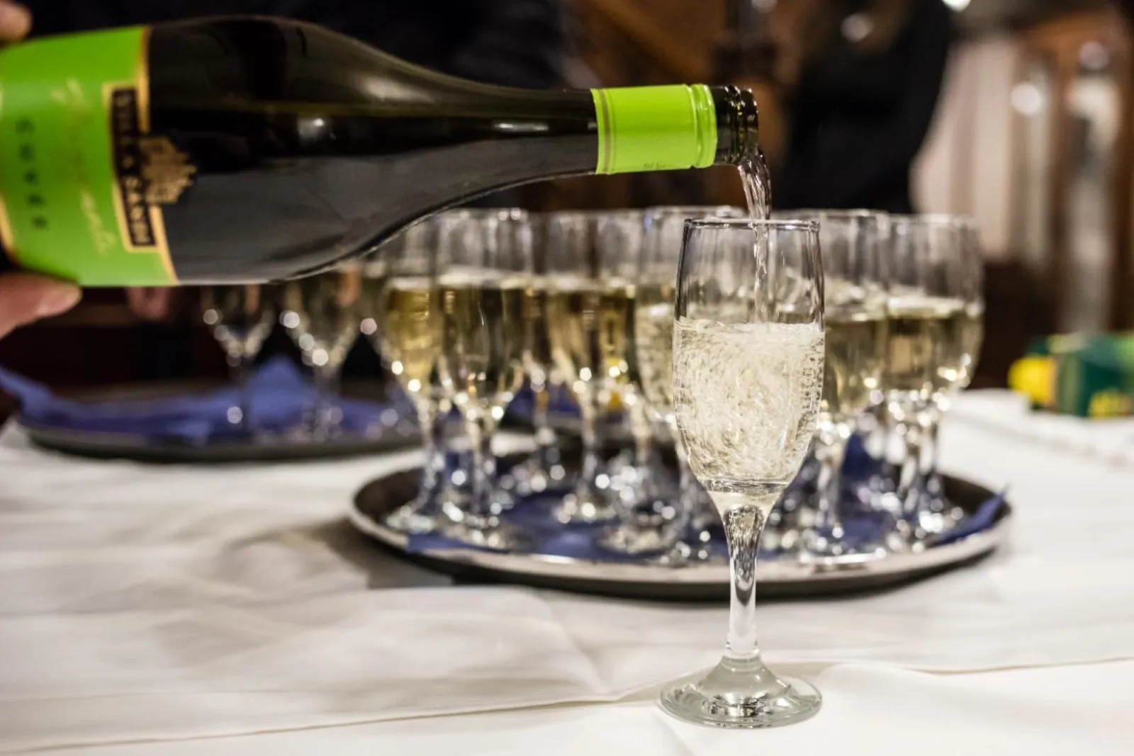 Sparkling wine poured into a tray of welcome-drink glasses on a white tablecloth