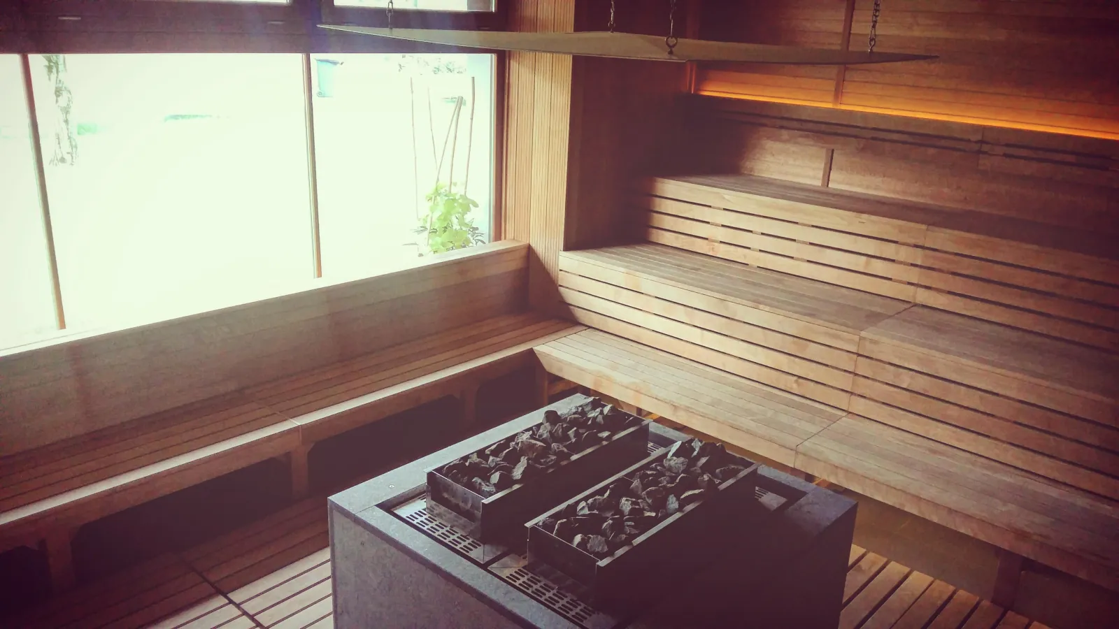 Wooden Finnish sauna at Paskál with tiered benches, a stone stove and a window
