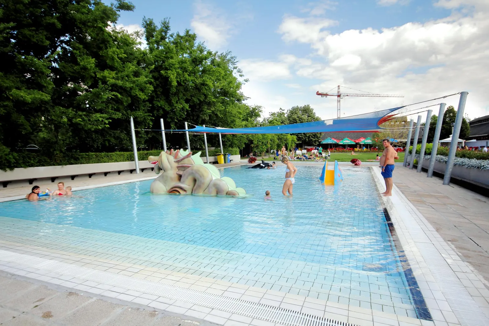 Outdoor children's pool at Paskál with a sculpted figure and a blue shade sail