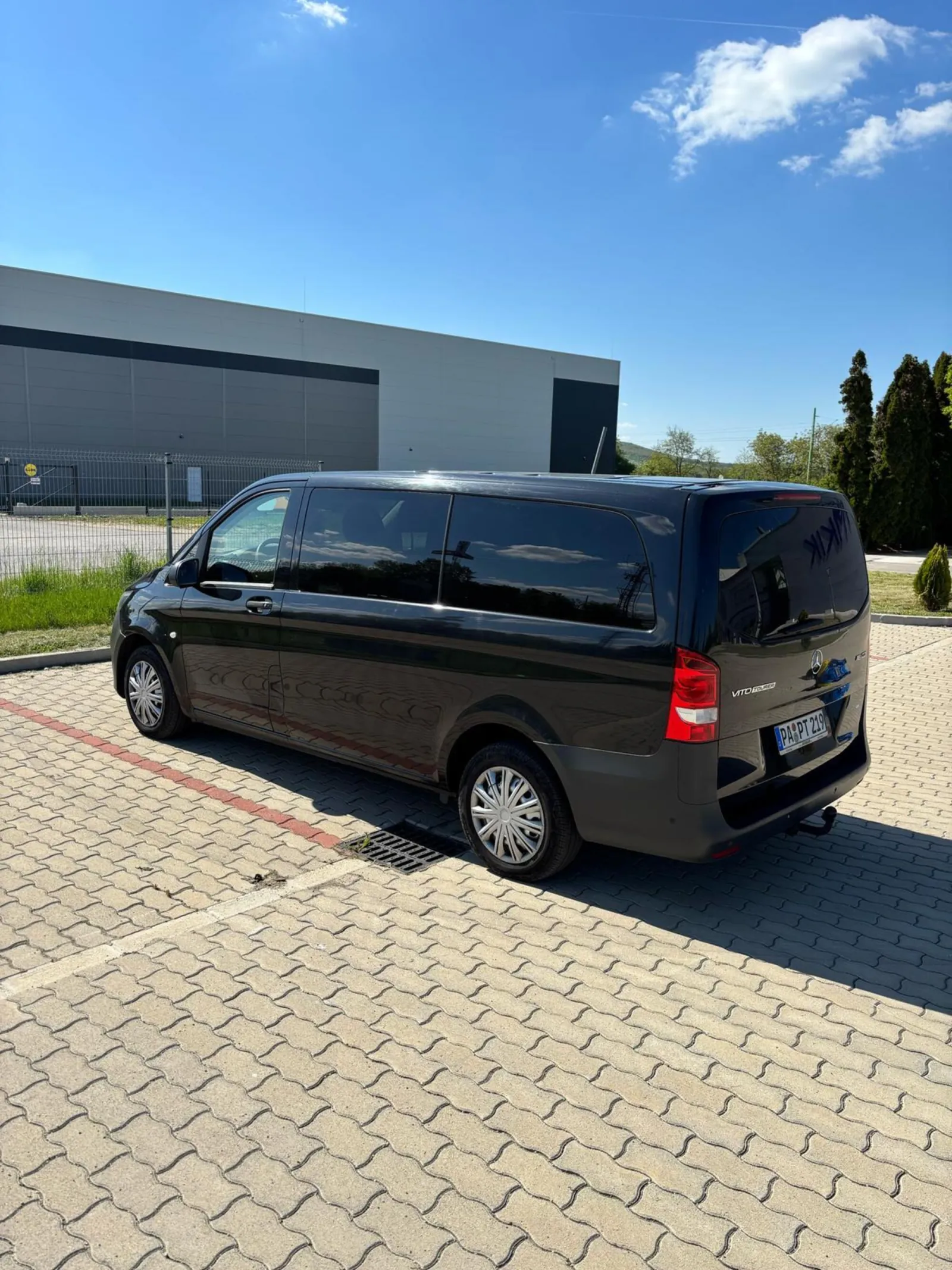 Black private transfer minivan parked on a paved lot under blue sky