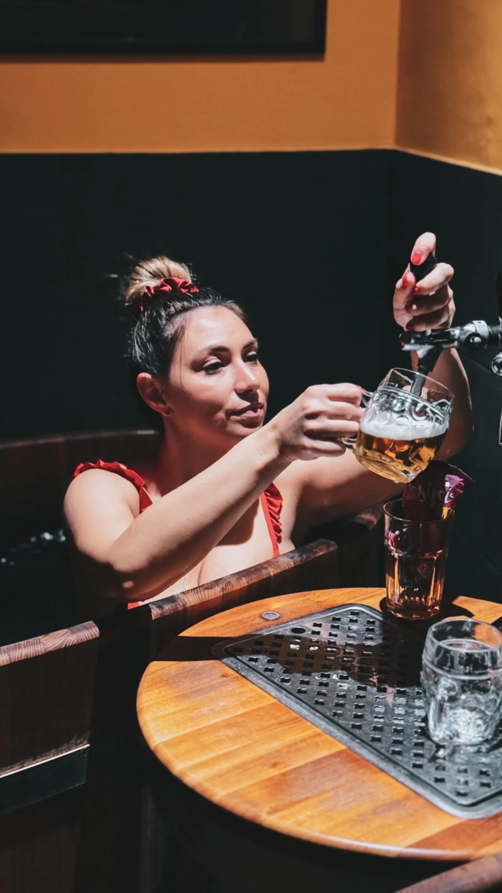 Woman in a wooden tub pulling her own draft beer from a tap at the beer spa