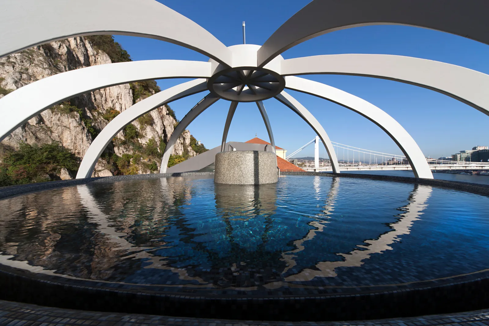 Round panorama pool under a white arched canopy, Gellért Hill cliffs and Elisabeth Bridge behind
