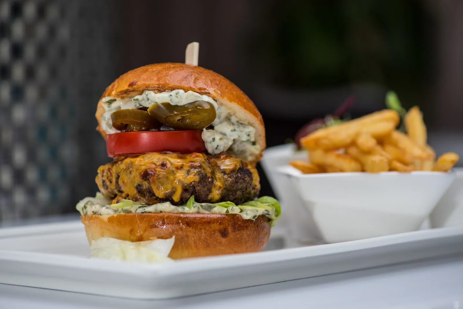 Rudas Bistro cheeseburger with jalapeños and tomato on a brioche bun, fries on the side