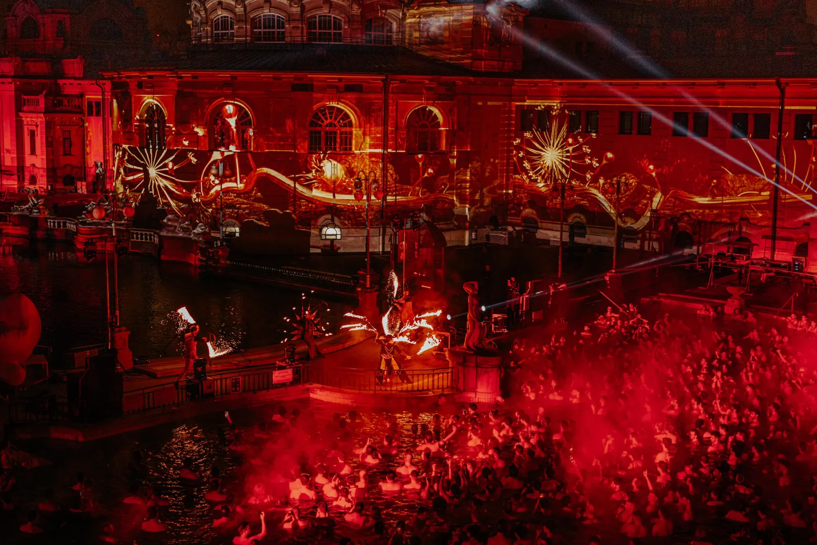 Red-lit crowd in the pool and projections on the bathhouse during Sparty