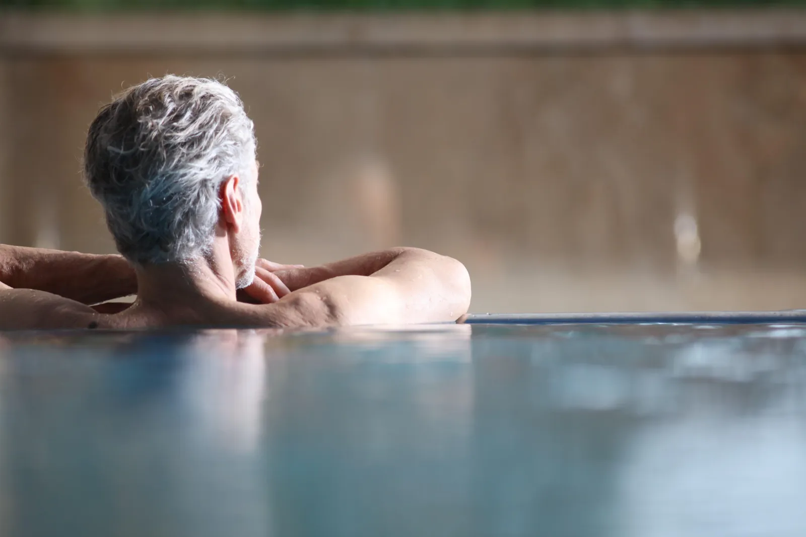 Grey-haired man resting his arms on the edge of an indoor pool