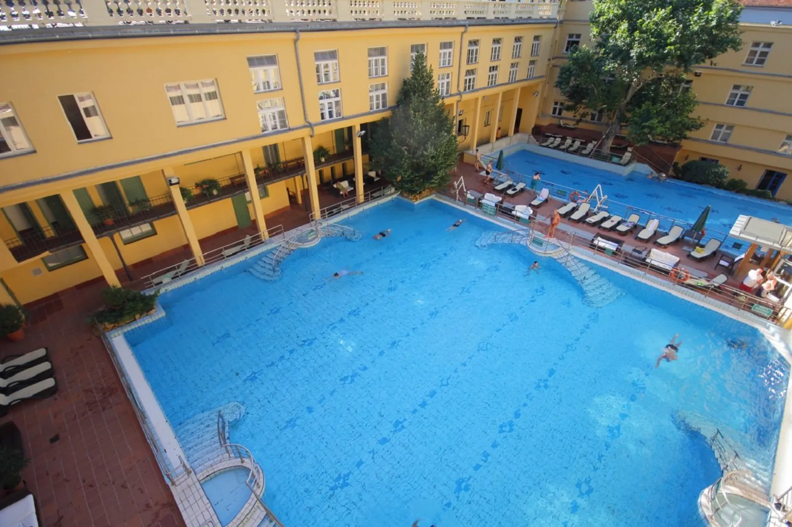 Aerial view of the Lukács outdoor pools with loungers along yellow arcaded courtyard walls