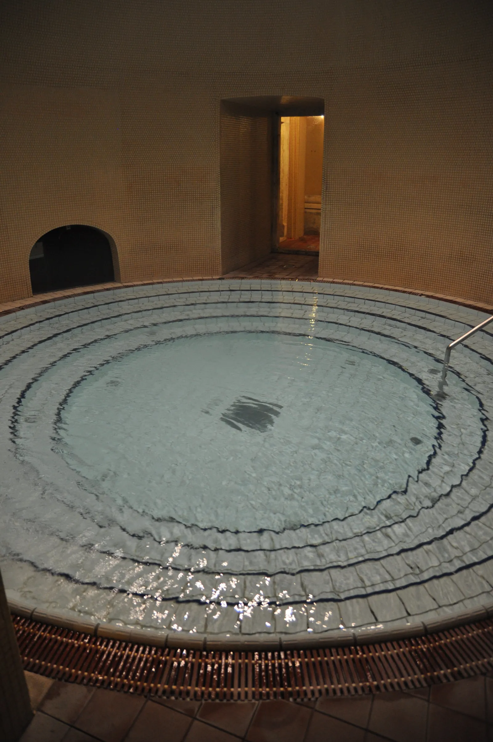 Round stepped indoor pool in a dim tiled room at the Lukács bath