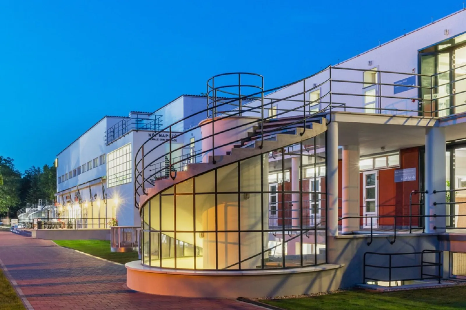 Modernist Palatinus building with a glazed spiral staircase lit at dusk