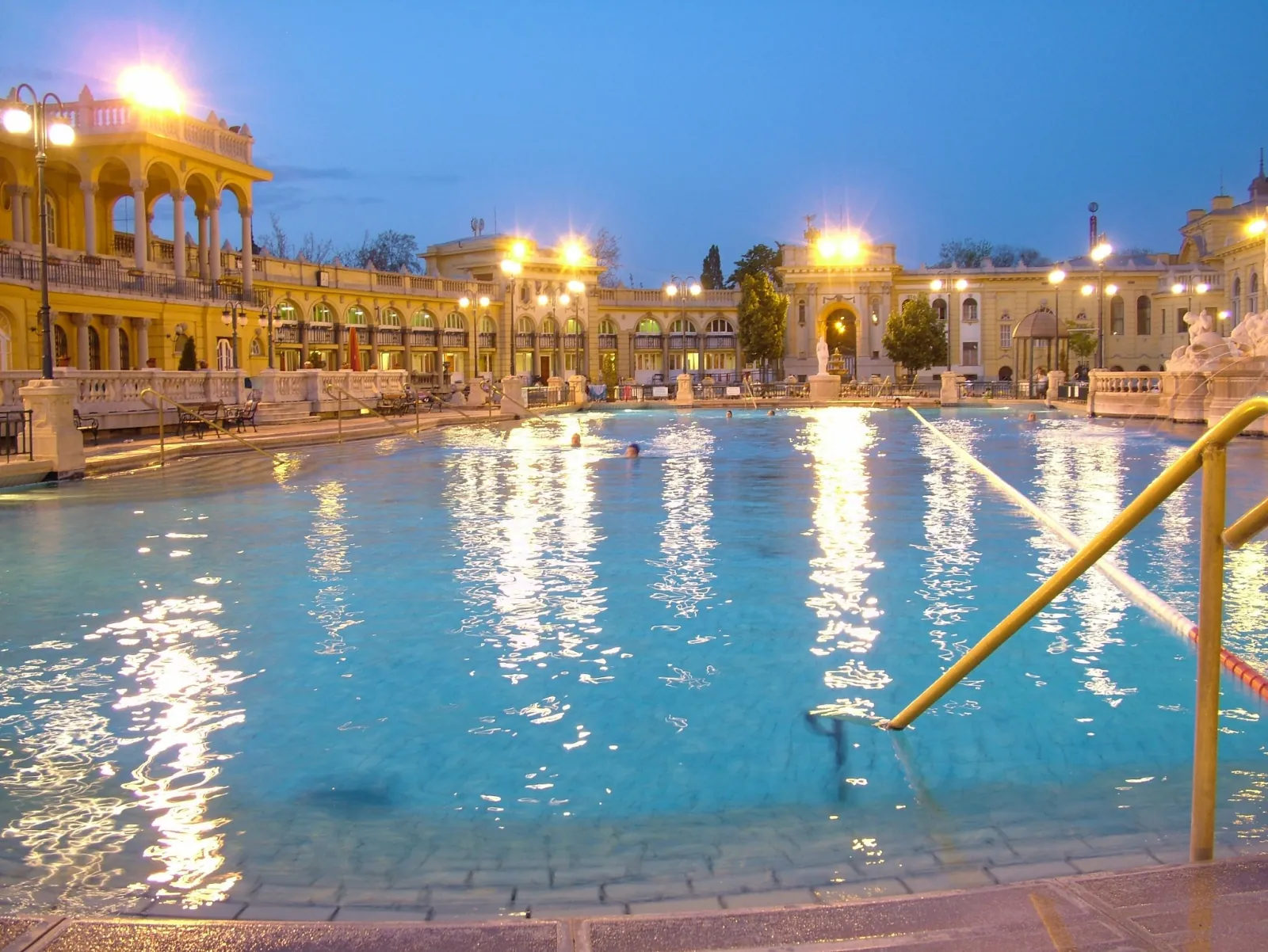 Széchenyi's outdoor swimming pool lit up at night with yellow facades behind