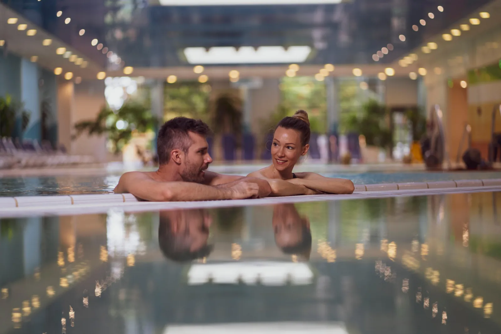 Couple leaning on the edge of the indoor swimming pool at the Helia spa