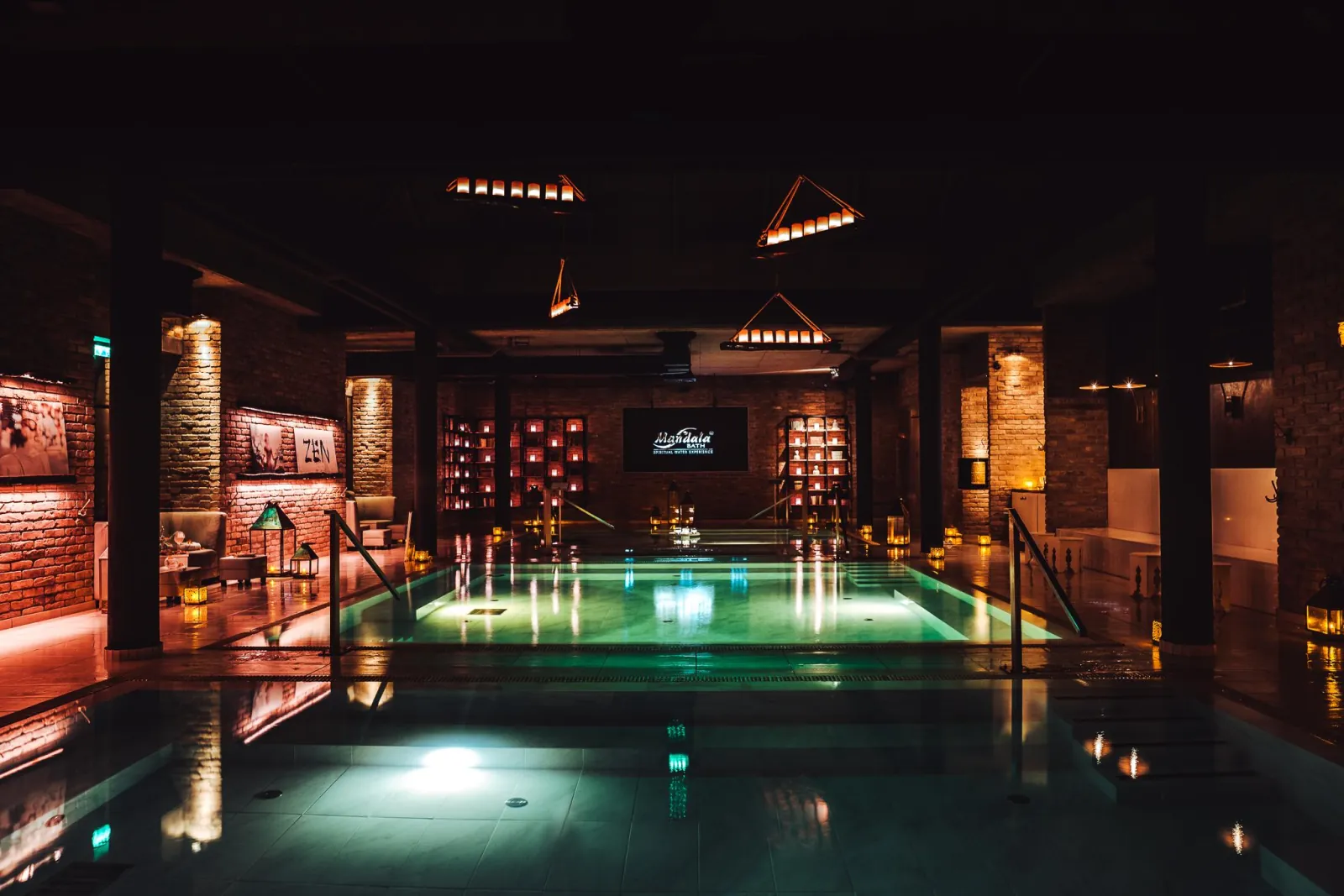 Mandala Day Spa's dim bath hall with glowing turquoise pools, brick pillars and hanging lanterns