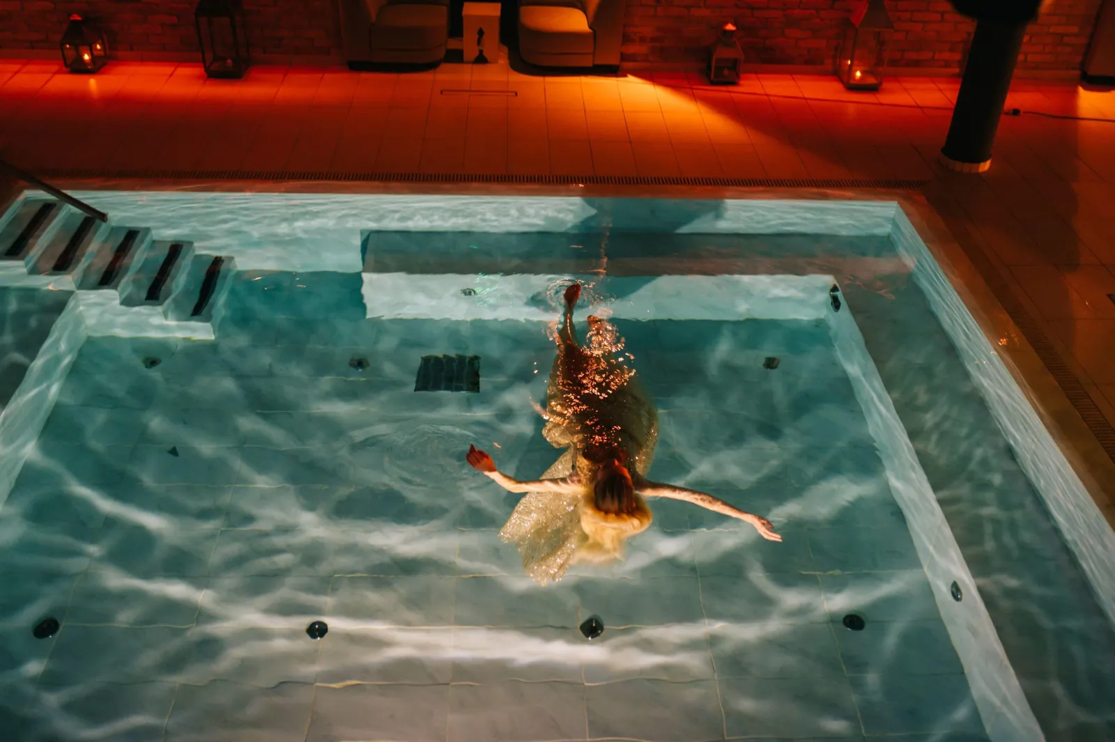 Swimmer in a flowing dress gliding through a lit Mandala pool with steps in the corner