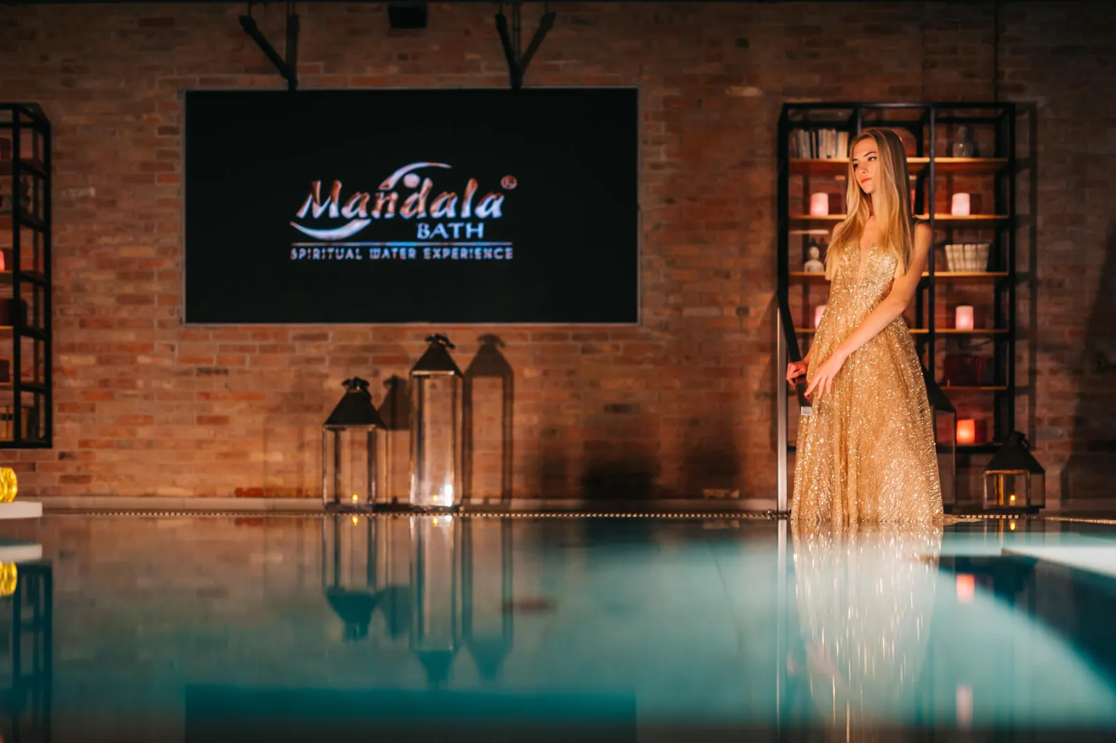 Woman in a gold gown by the pool under the Mandala Bath Spiritual Water Experience sign