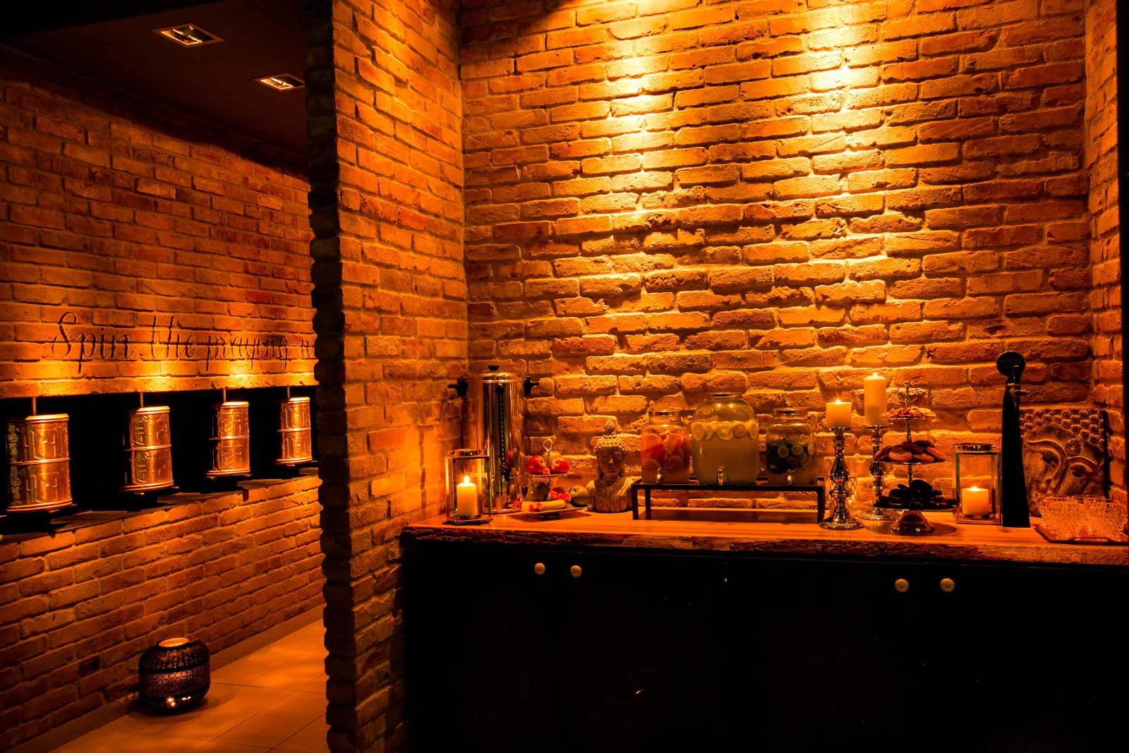 Candlelit brick-walled tea corner with brass urns, glass jars and lanterns at Mandala