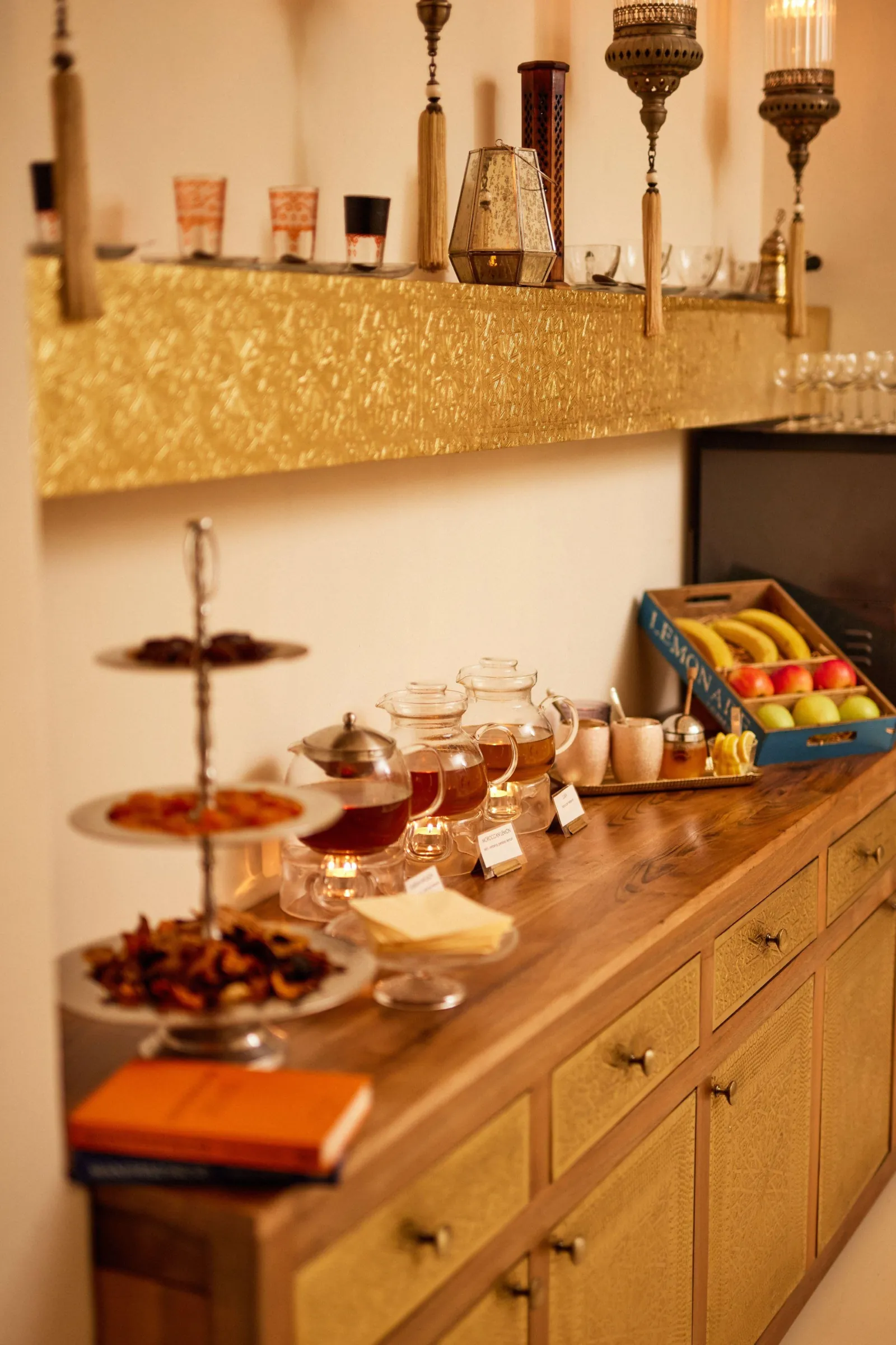 Tea bar with glass teapots, dried fruit on tiered stands and a basket of fresh fruit