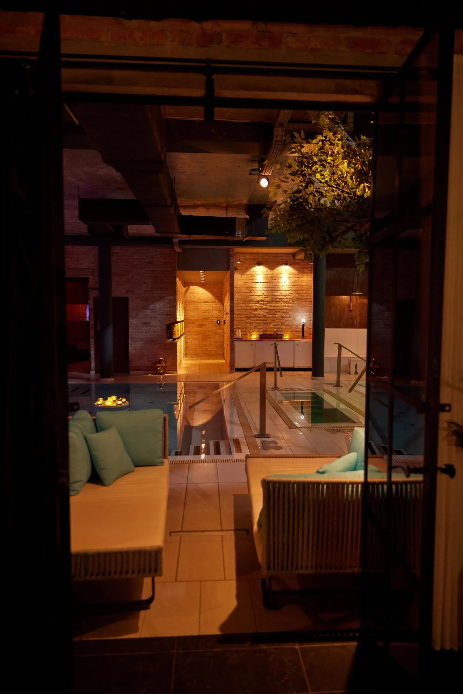 Cushioned lounge seating and a lit pool seen through a dark doorway at Mandala Day Spa