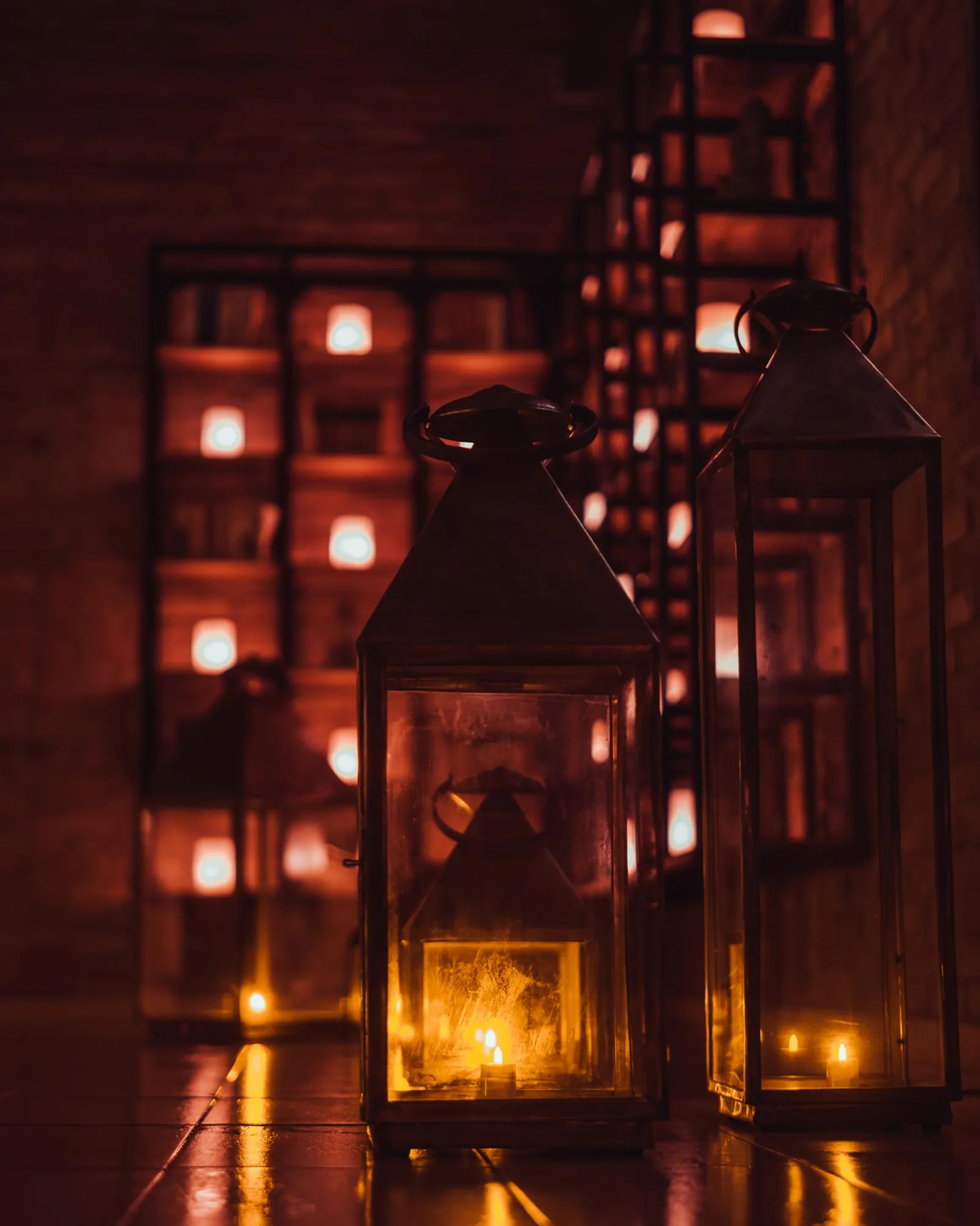 Glowing lanterns on a dark floor in front of a candlelit brick wall