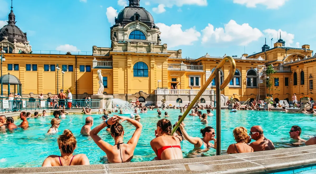Bathers in the outdoor thermal pool at Széchenyi Baths under the yellow domed bathhouse on a sunny day