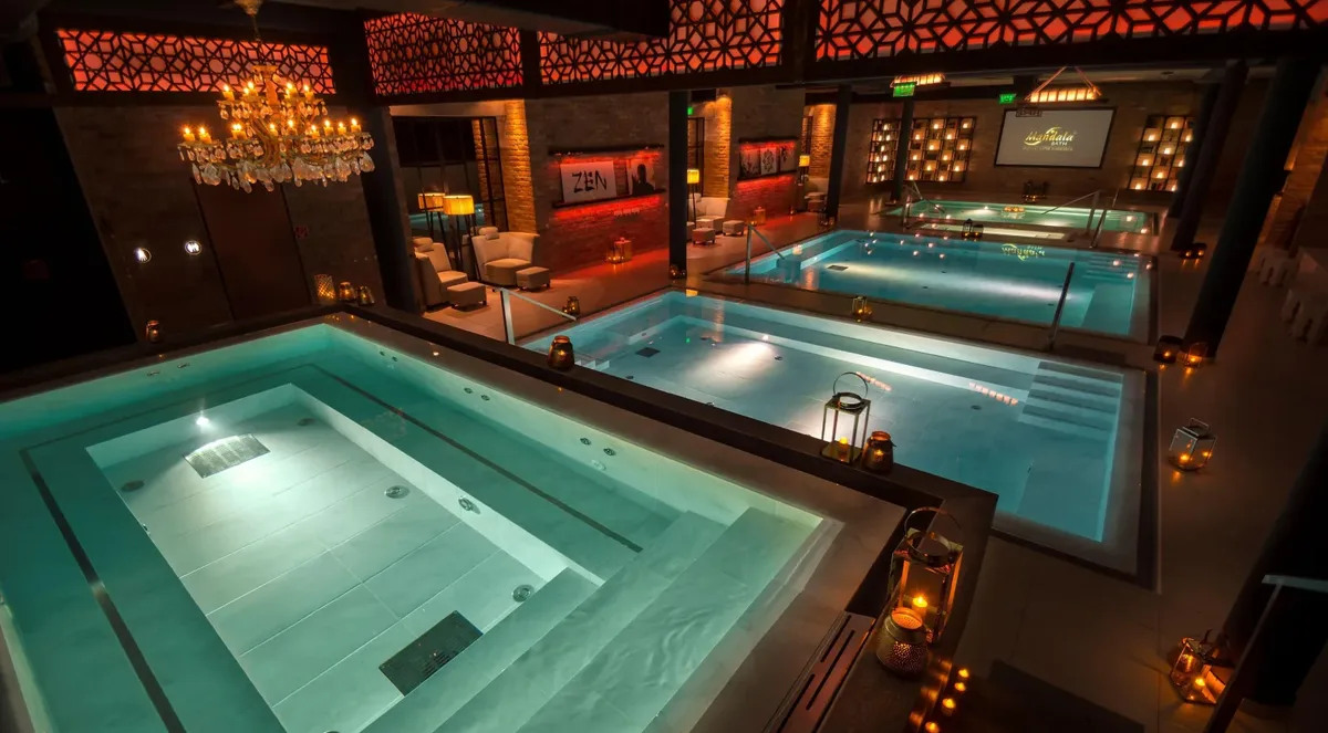 Candle-lit indoor pools at Mandala Day Spa under a crystal chandelier, with red lattice panels and brick walls around them