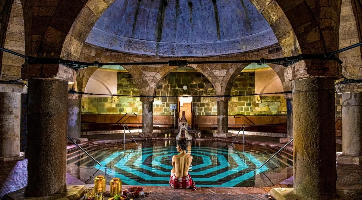Octagonal thermal pool lit blue under the stone dome and columns of the Rudas Turkish bath