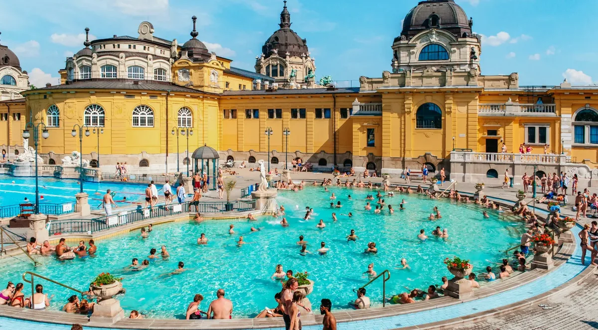 Crowded outdoor thermal pool at Széchenyi Baths seen from above, with the domed yellow bathhouse behind